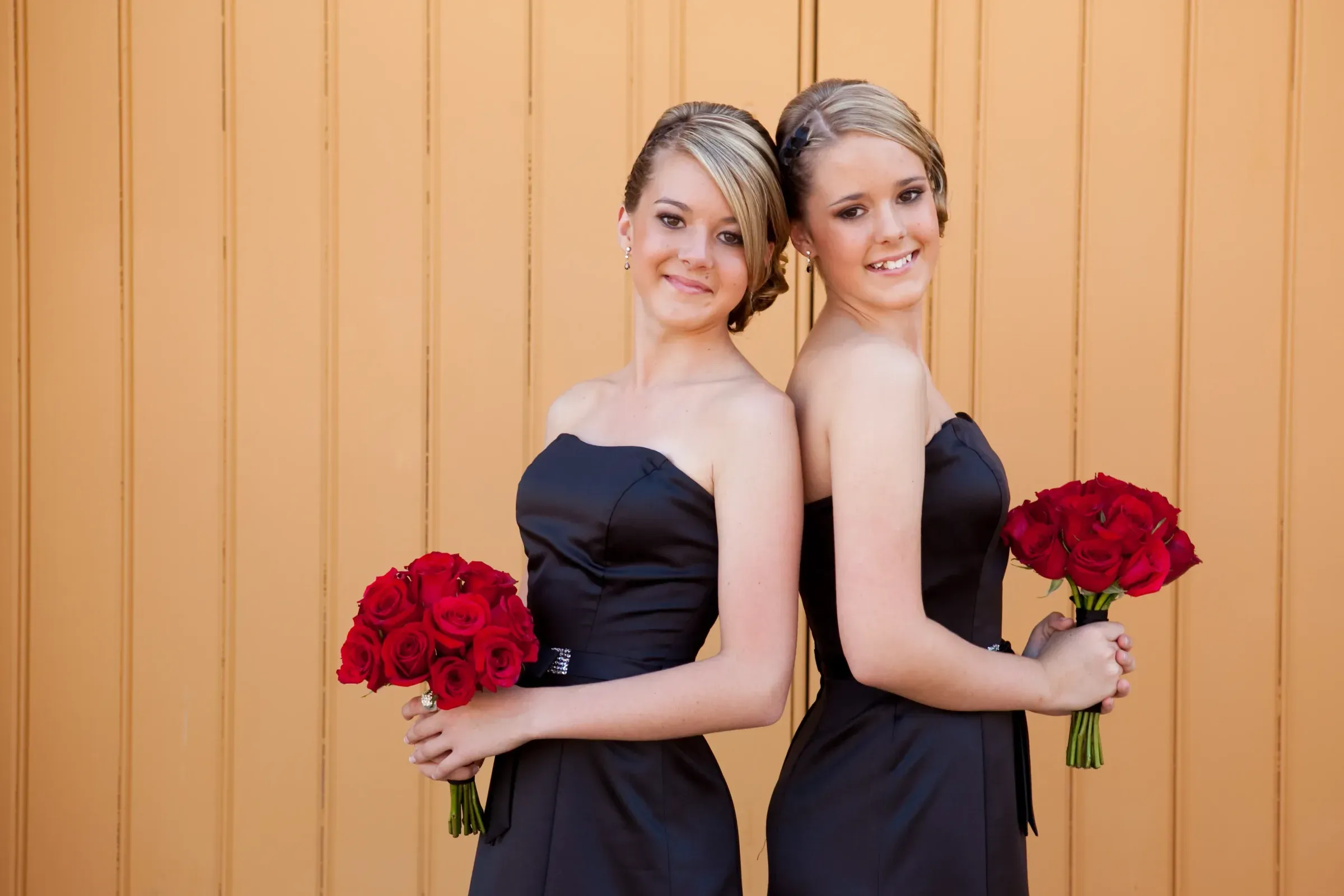 Two bridesmaids holding deep red bouquets, hair and makeup by Bellus