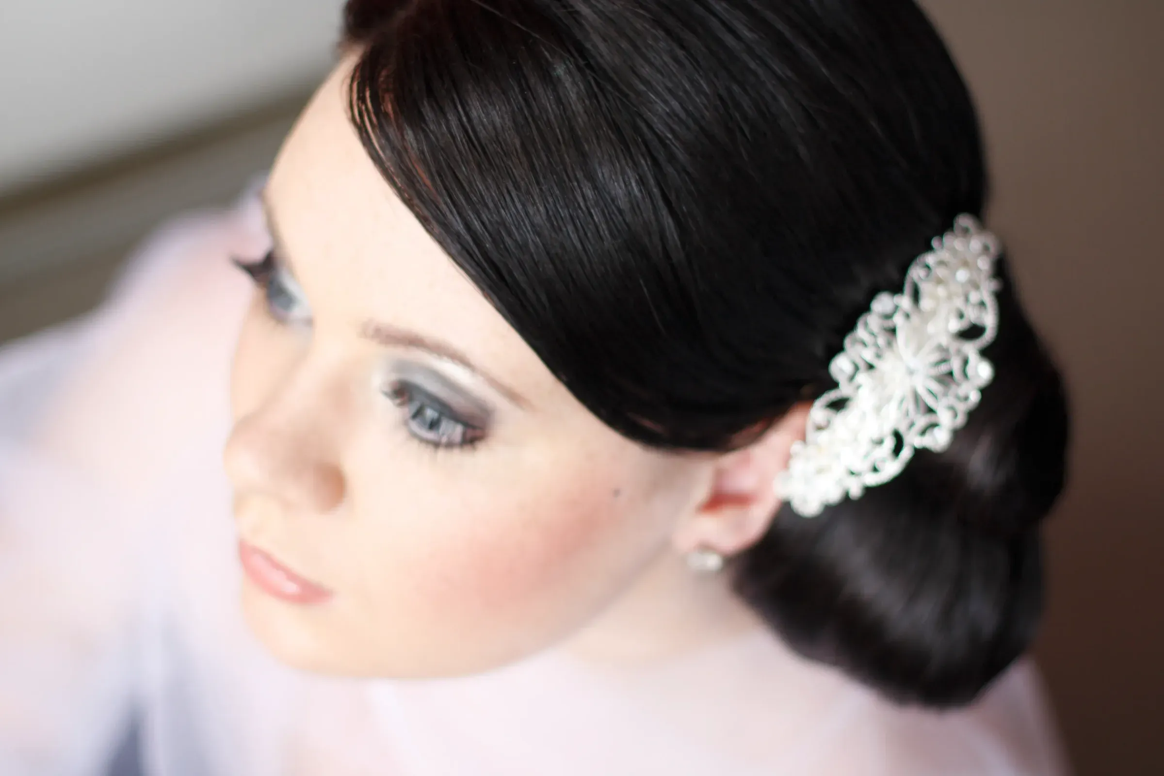 A finished classic bridal face, sleek dark chignon dressed with a jewelled comb and a precise liner