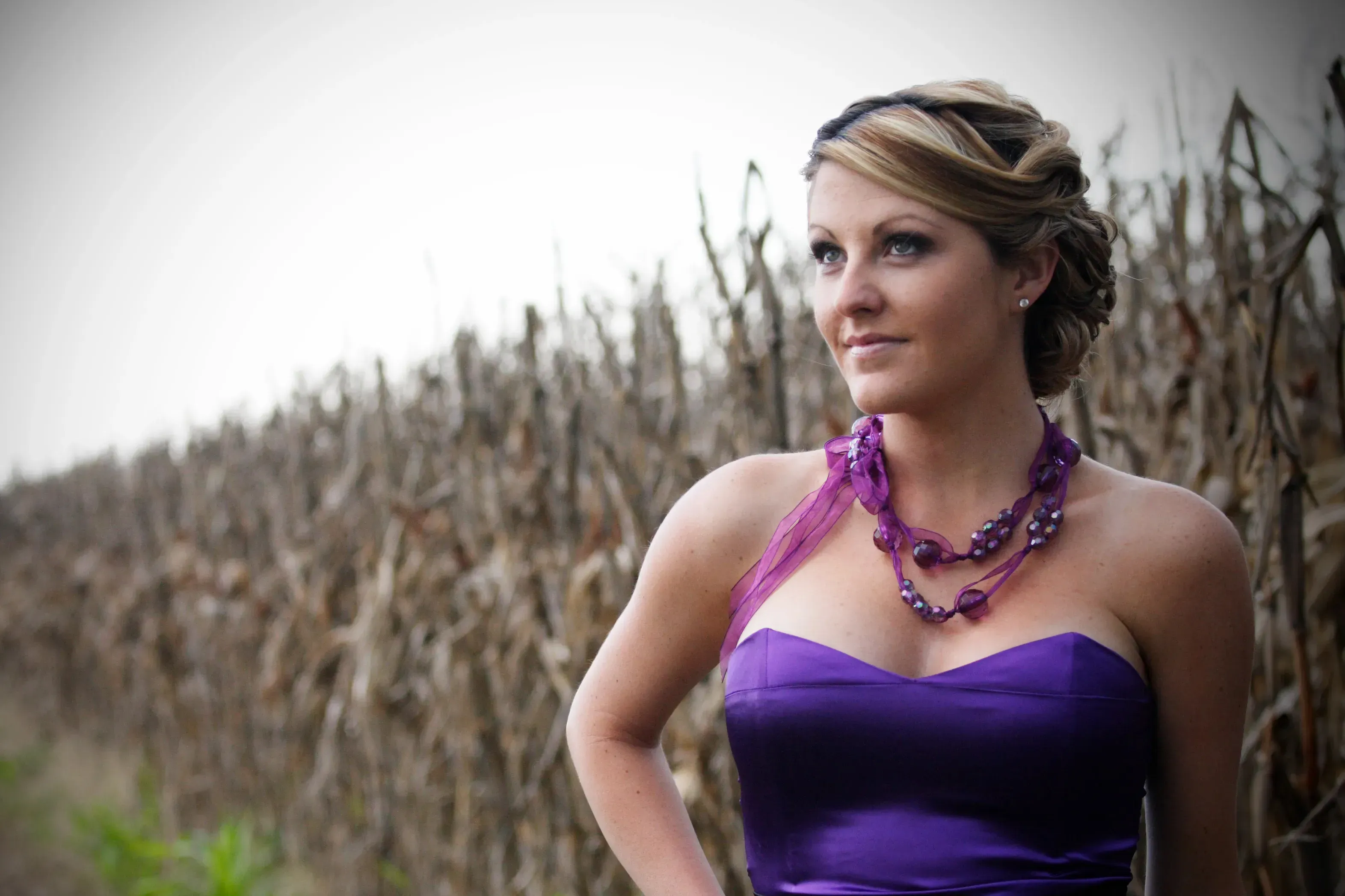 A woman in a purple gown with a sculpted updo and long-wearing makeup, styled by Amanda Frost for a day at the races