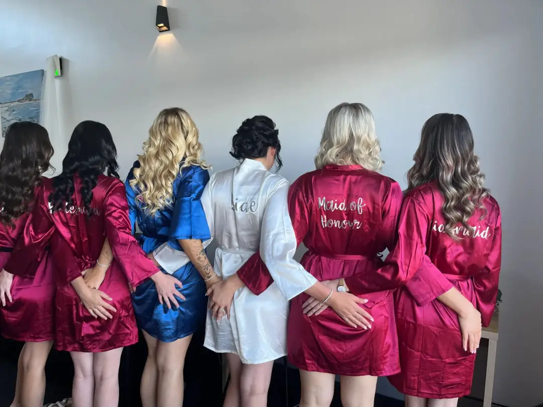 Bride and five bridesmaids in monogrammed robes from behind, hair styled and ready