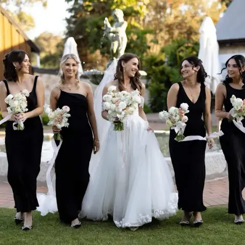 Bride walking with her bridesmaids in black, hair styled long and pinned back across the party