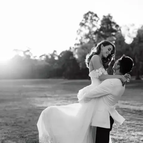 Groom lifting his bride in a paddock at sunset, her long hair worn down in soft waves