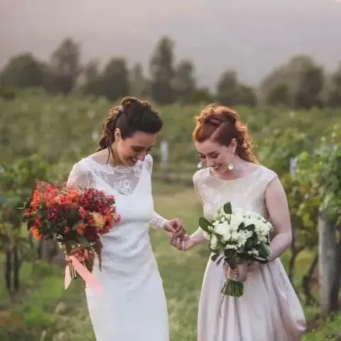 Two brides in a vineyard at dusk, one with a braided updo and one with red hair pinned back