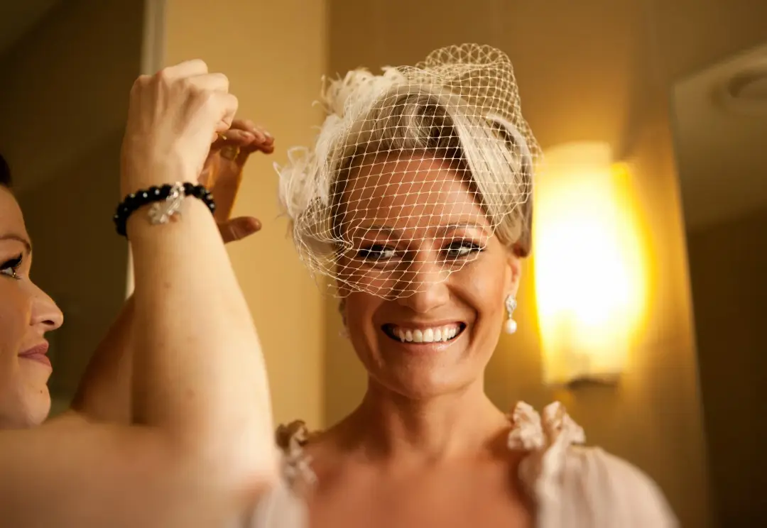Bride laughing as her birdcage veil is pinned into place on the wedding morning