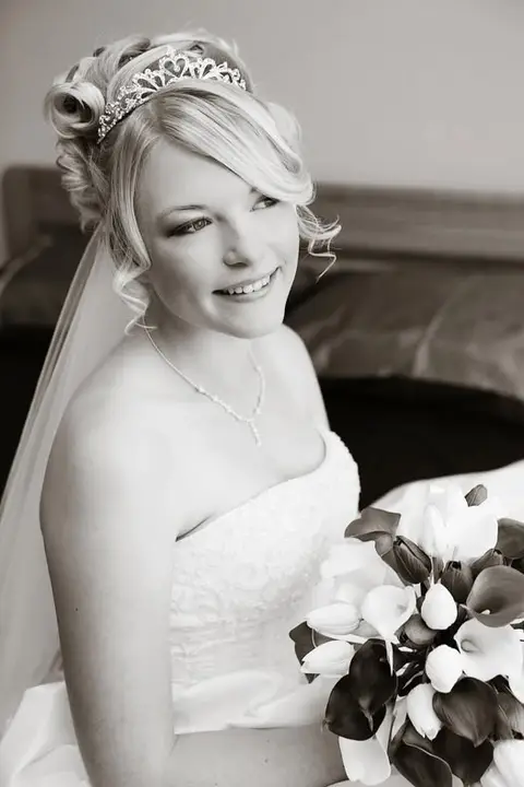 Bride in a tiara and veil with her blonde hair curled and pinned, holding calla lilies