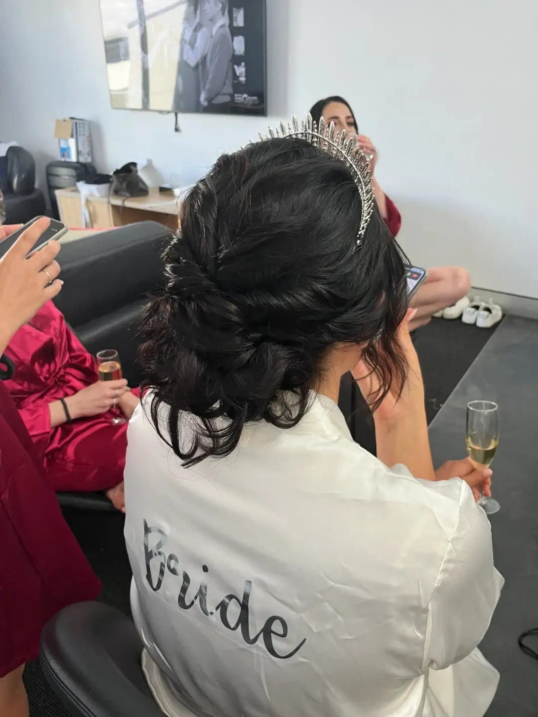 Bride in a white robe wearing a tall tiara, her dark hair pinned into a textured low updo