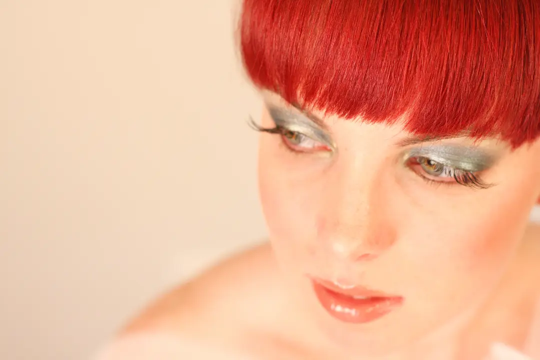 Aqua and gold eye makeup with a heavy lash, styled with a blunt red fringe
