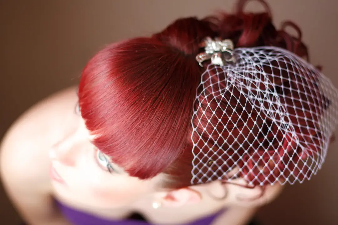 Deep red hair rolled into a vintage updo and dressed with a birdcage veil and diamante clip