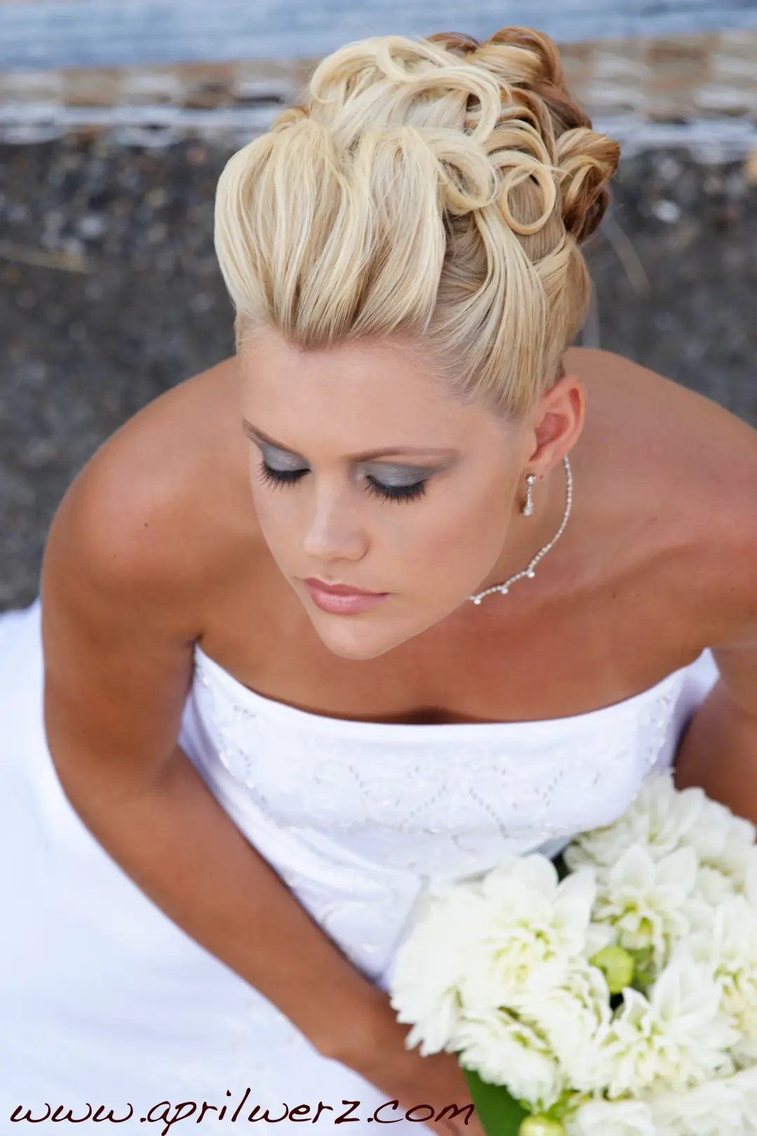 Bride looking down at a white bouquet, her blonde hair set in a curled high updo