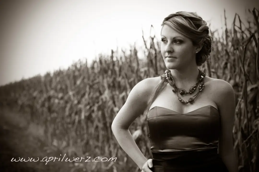Guest in a strapless gown beside a cornfield, her hair swept into a braided updo