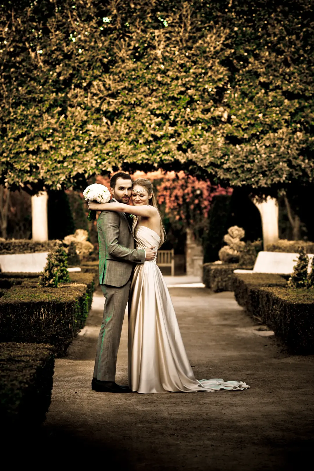 Bride and groom in a hedged garden, her hair worn long and smooth with a satin gown