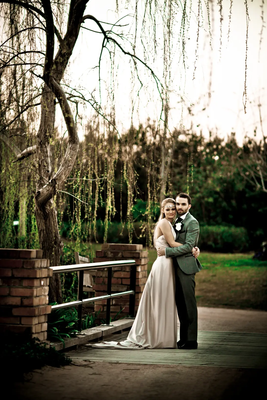 Bride and groom on a bridge under a willow, the bride's hair worn in a low pinned style