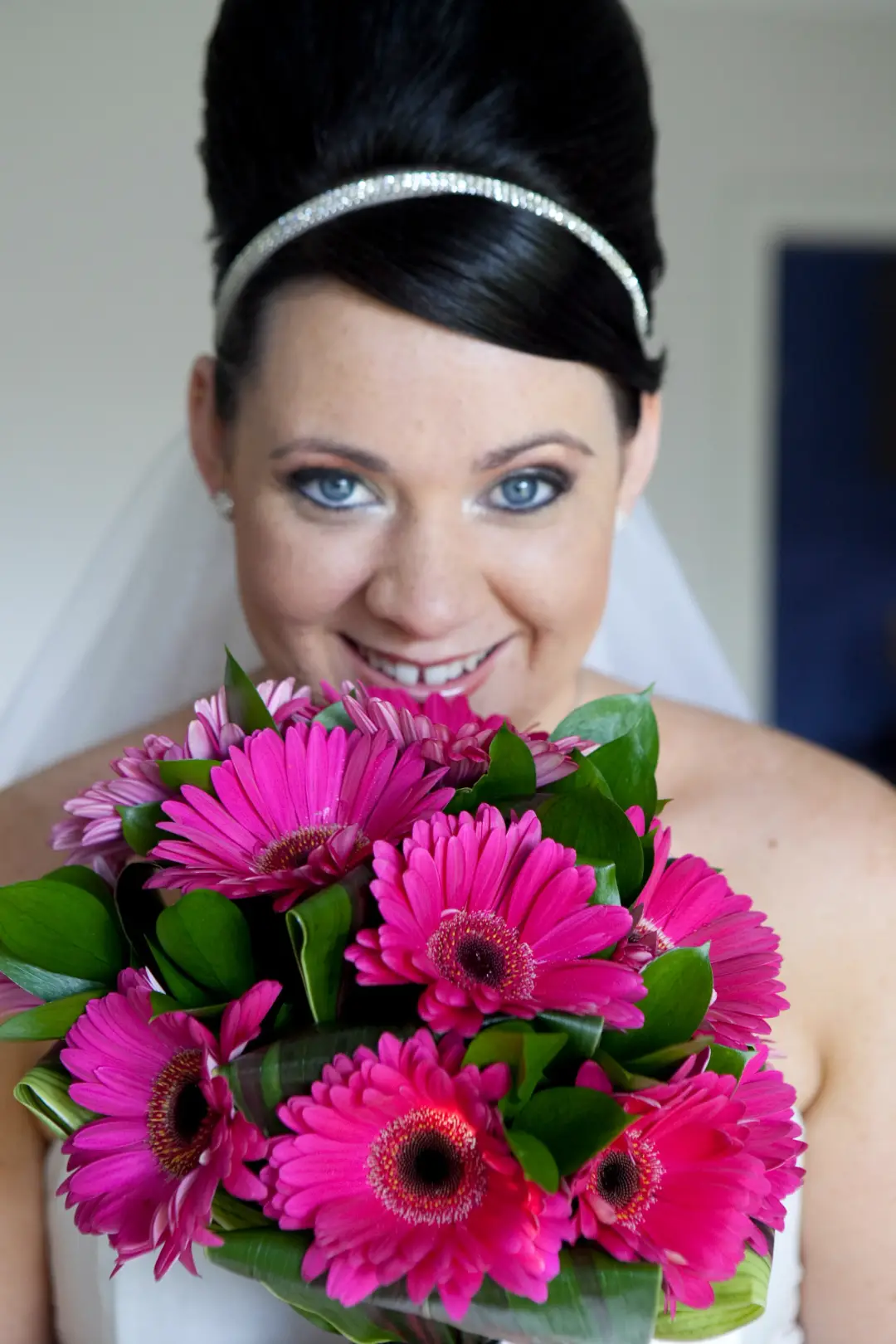 Bride in a dark high updo with a diamante headband and veil, holding pink gerberas