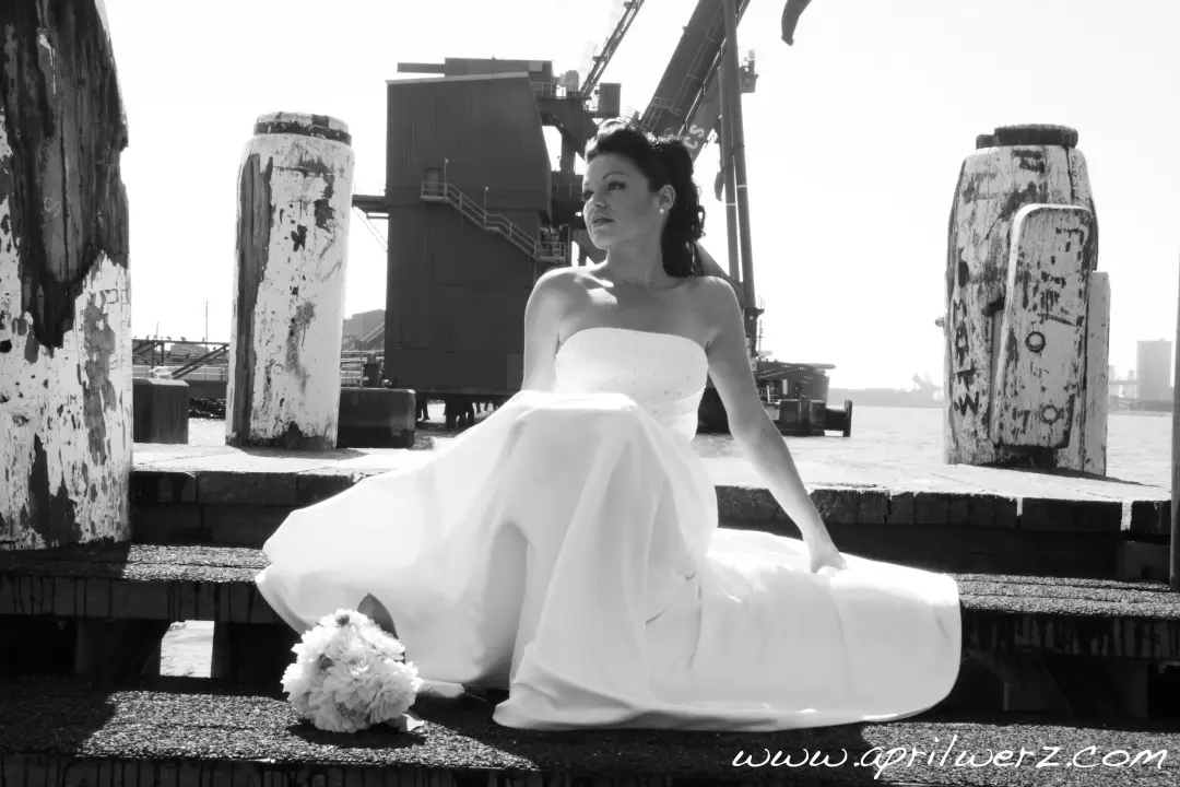 Bride seated on a wharf in a strapless gown, her dark hair pinned into a low knot