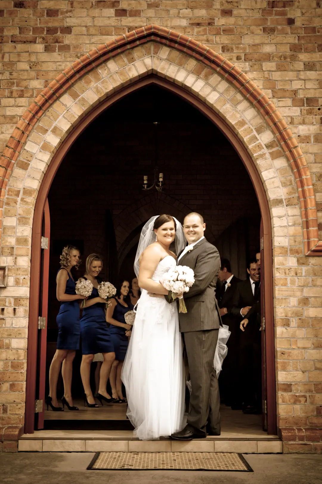 Bride and groom in a church archway, the bride's dark hair pinned back under a full veil