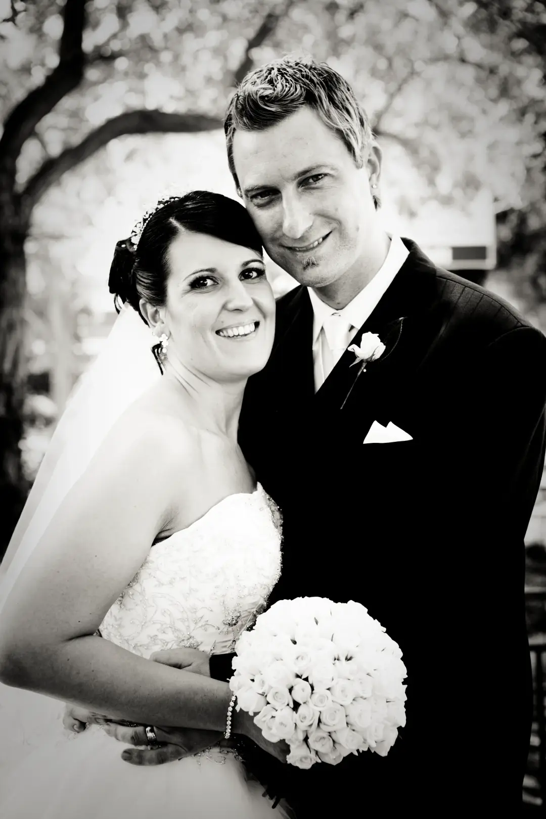 Bride and groom under a tree, her dark hair pinned into a low style with a jewelled clip
