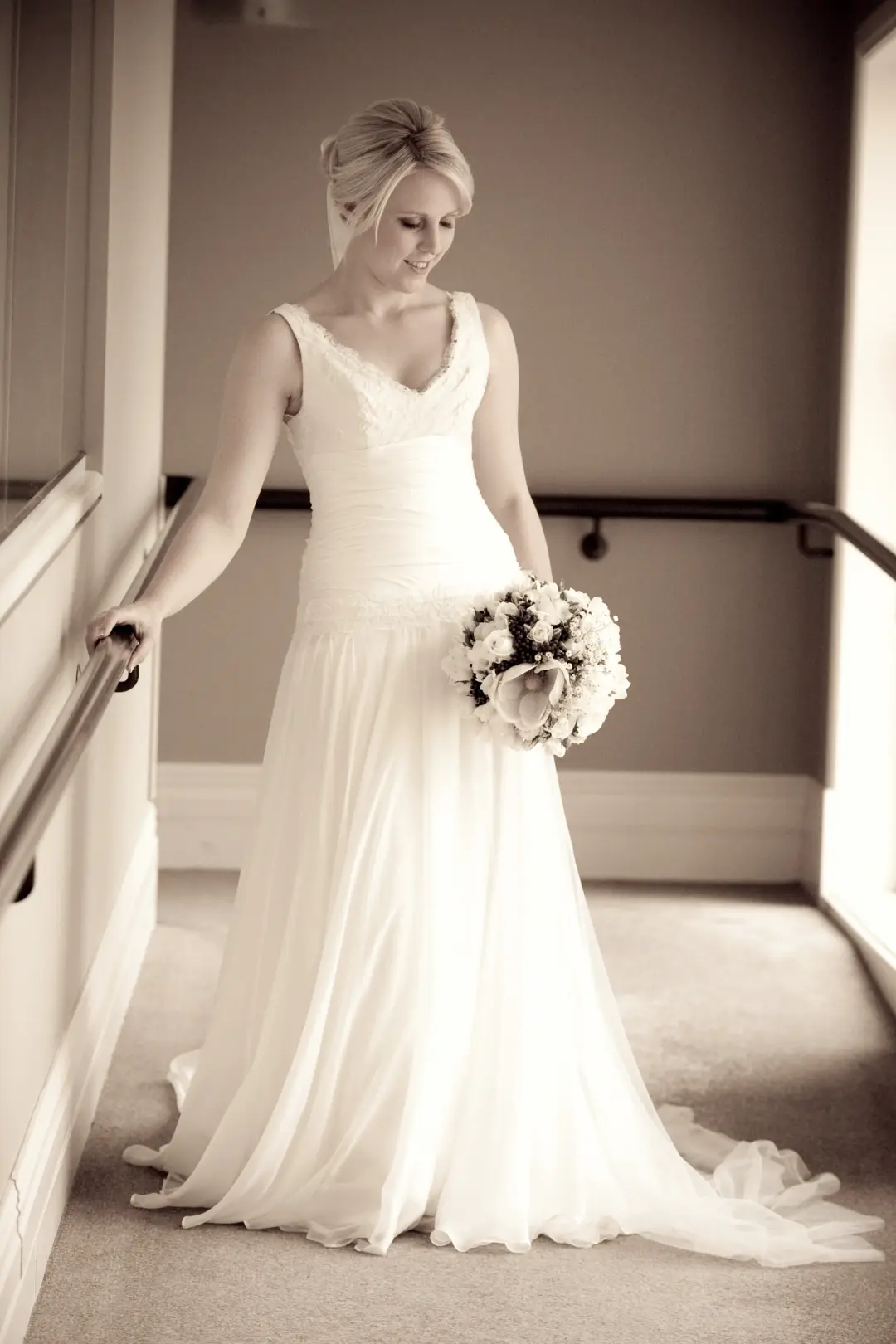 Bride on a landing in a chiffon gown, her blonde hair pinned up with soft tendrils left out