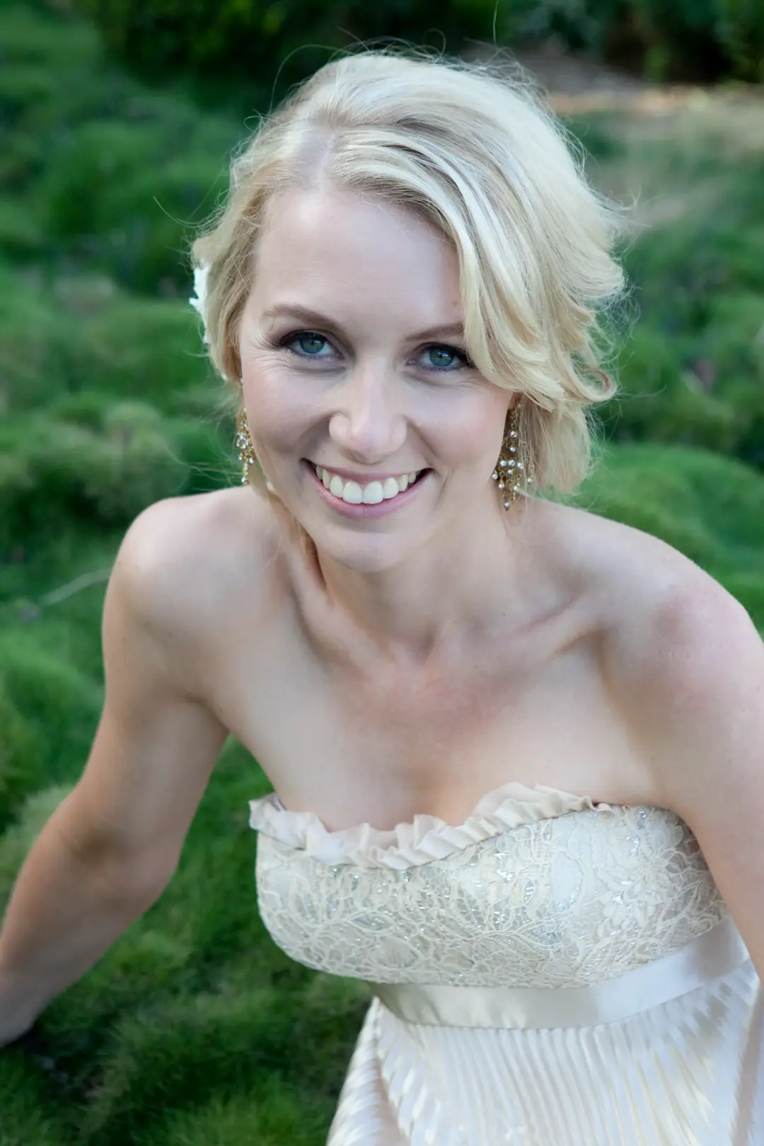 Bride in a soft blonde updo with tendrils left loose, wearing a lace gown and chandelier earrings