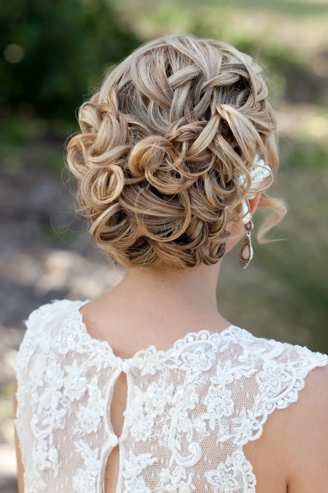 Back view of a curled and braided upstyle pinned with a pearl hairpiece above a lace gown
