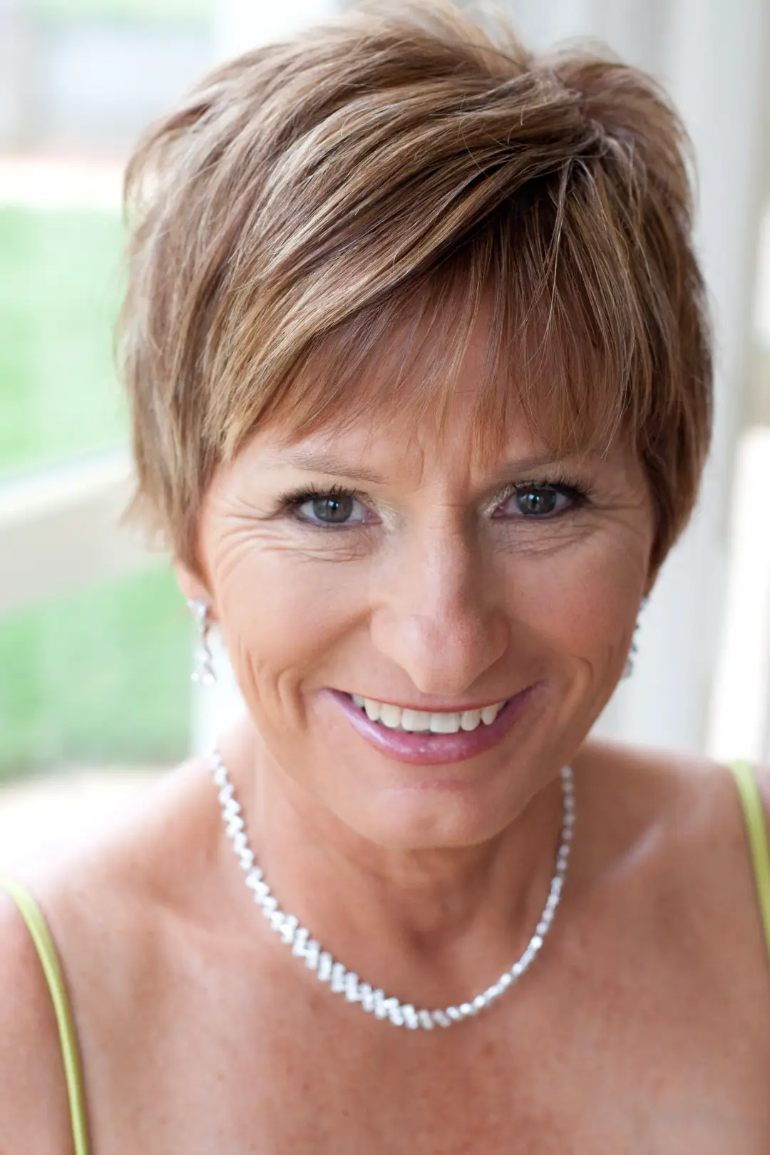 Mother of the bride with a short layered blonde cut, wearing soft finished makeup and pearls