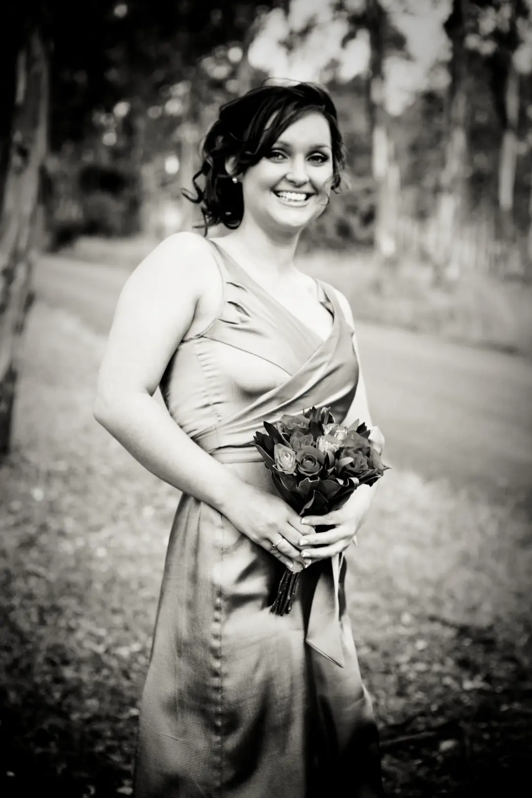 Bridesmaid in satin with her dark hair pinned into a soft updo, holding a small posy
