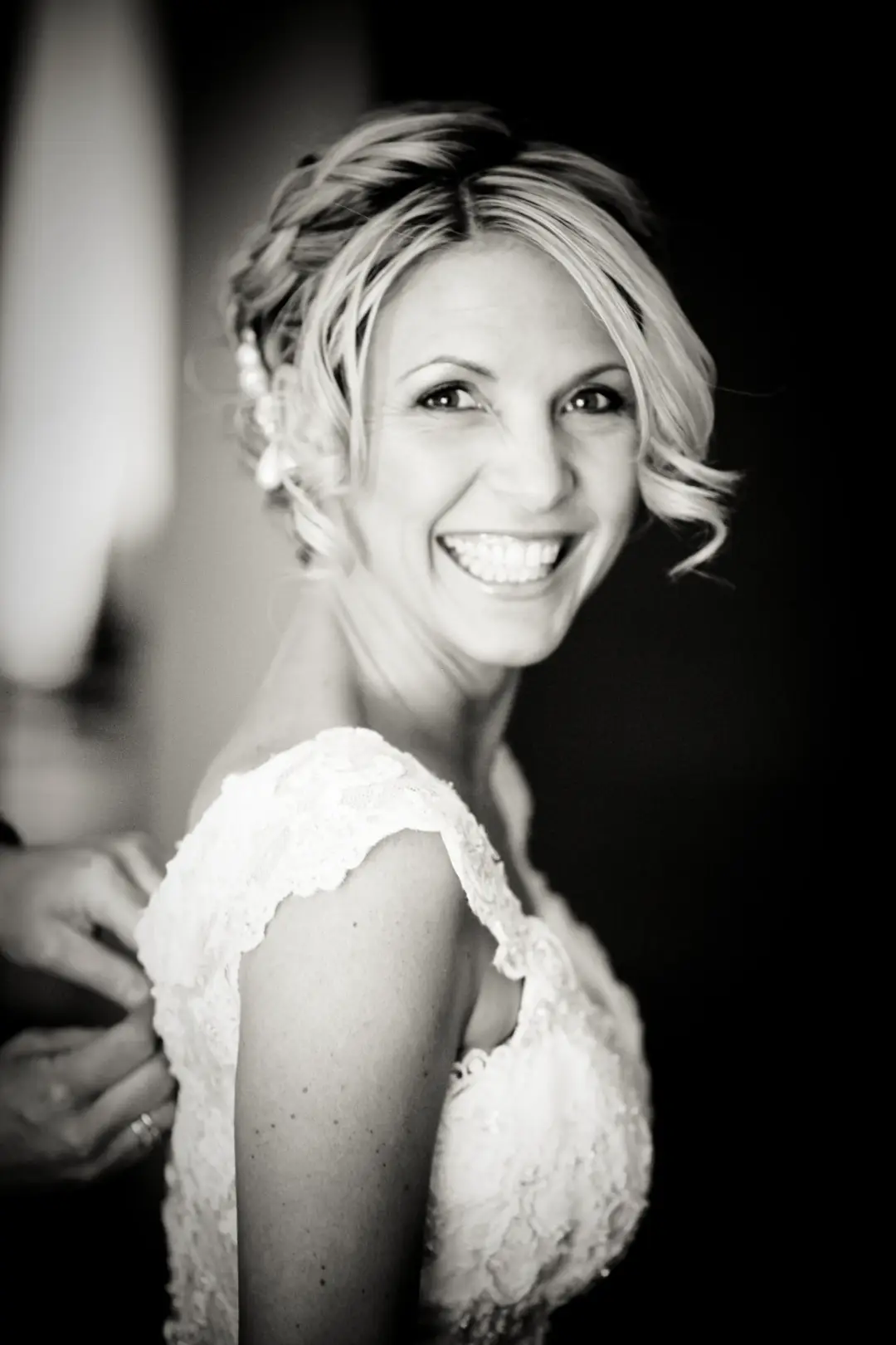 Bride laughing as her gown is fastened, her blonde hair pinned into a braided updo