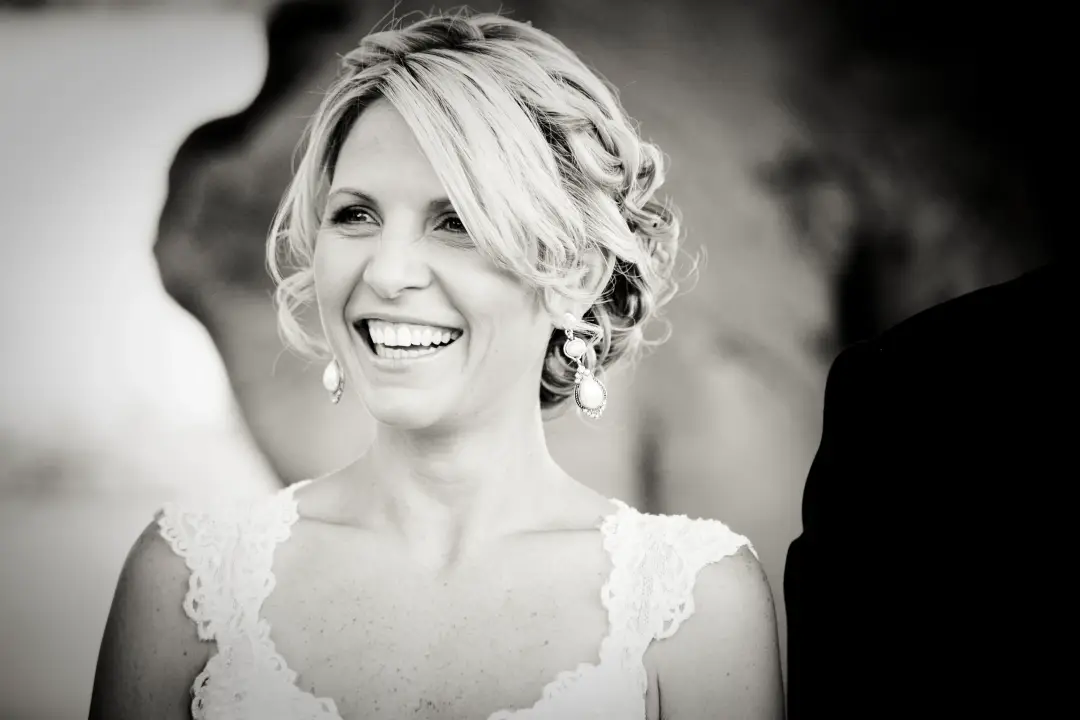 Blonde bride laughing in a soft curled updo, wearing a lace gown with cap sleeves