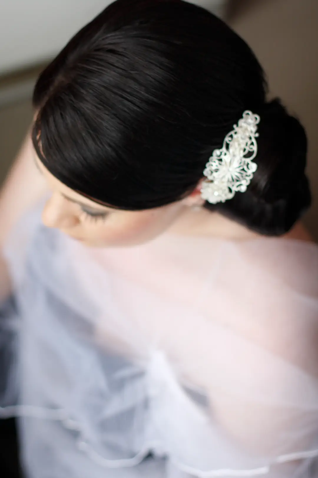 Dark hair pinned into a smooth low chignon with a lace hair comb, worn under a soft veil