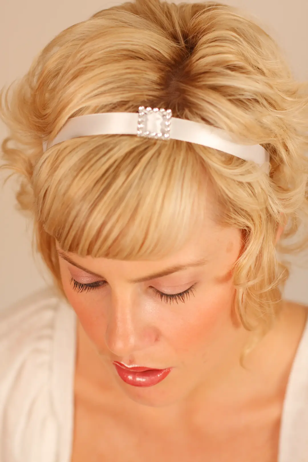 Short blonde hair styled with volume at the crown and a satin headband with a pearl clasp