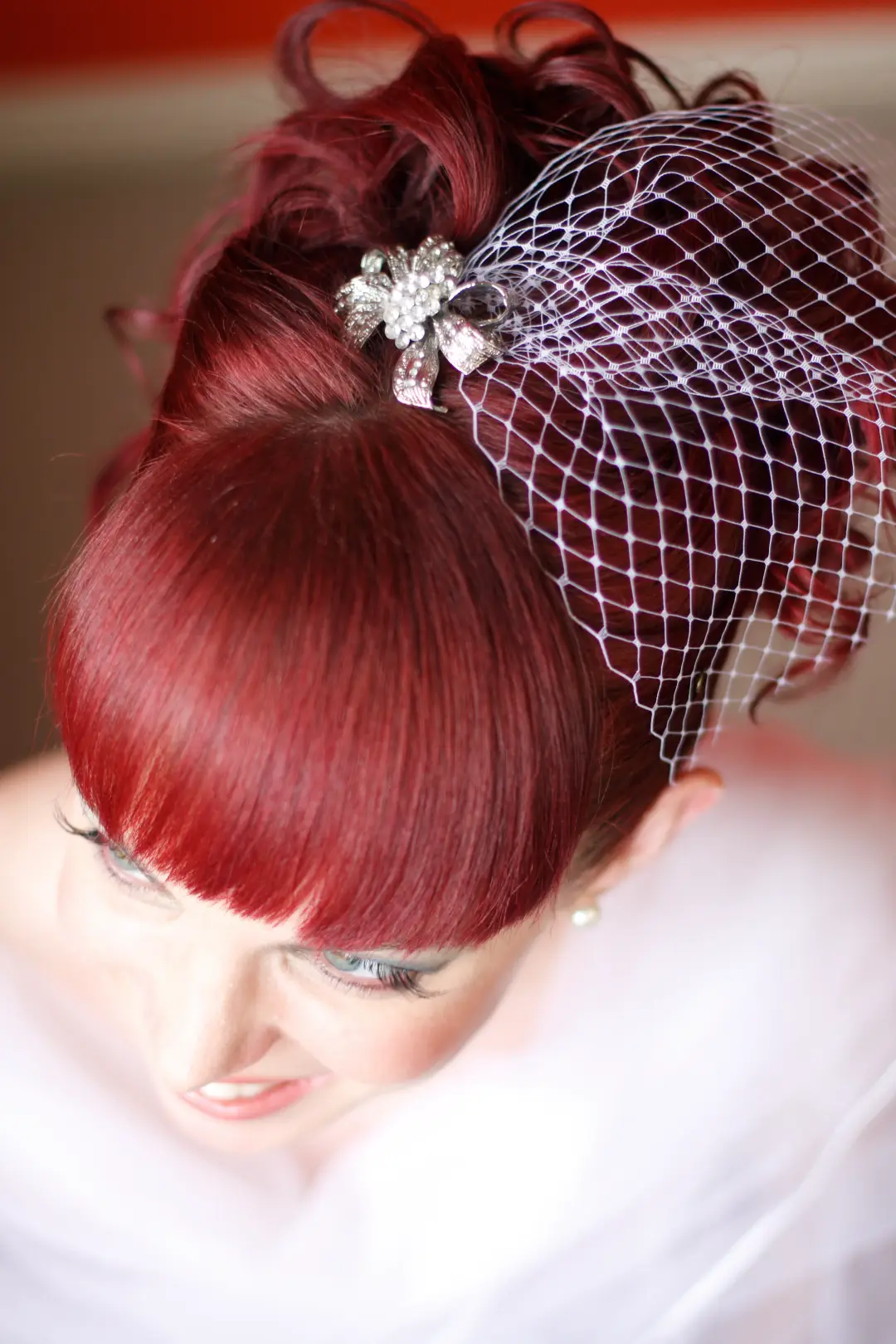 Red hair in a high curled updo with a birdcage veil and a diamante brooch
