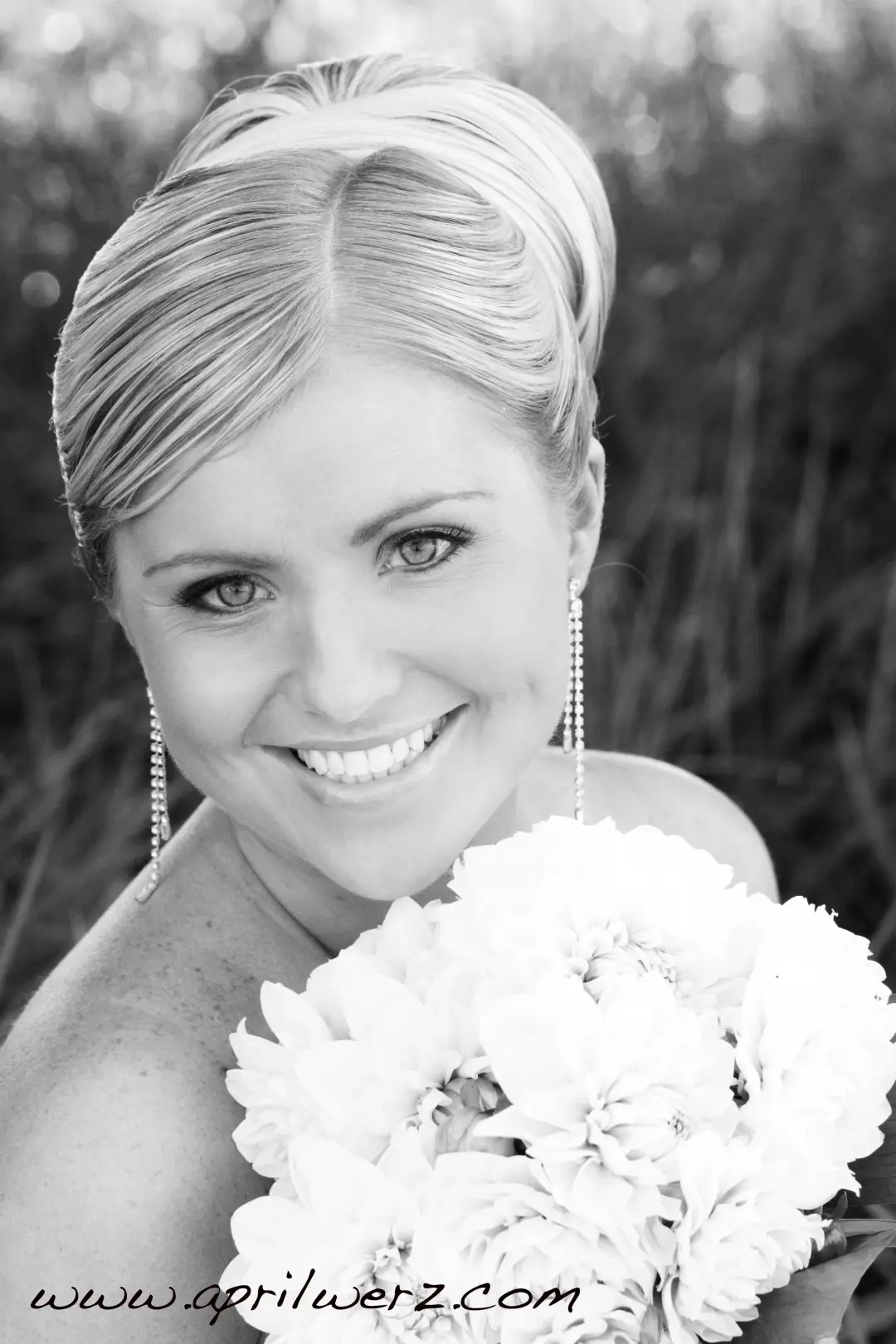 Bride with a short blonde style swept back, wearing long drop earrings and holding white blooms