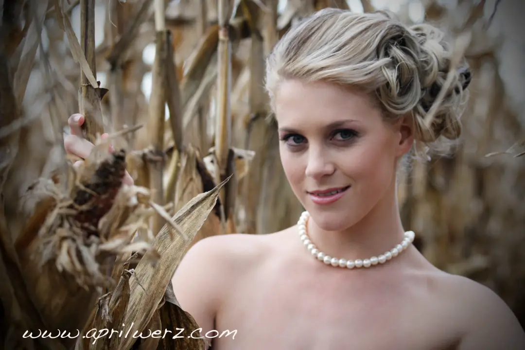 Portrait in a cornfield, blonde hair twisted into a rolled updo and worn with pearls