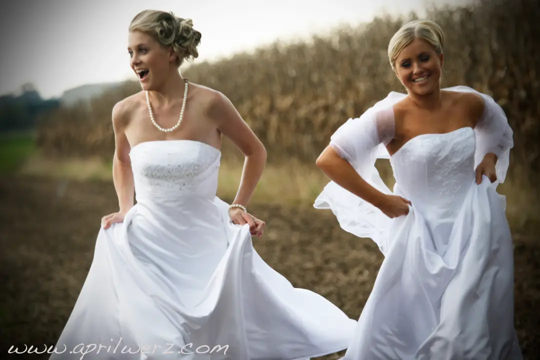 Two brides laughing in a field, one in a curled updo and one in a short blonde style