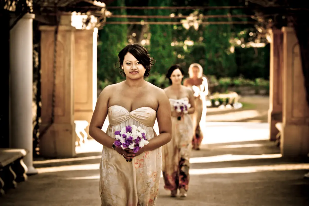 Bridesmaids walking down a garden colonnade, each with her hair styled up for the ceremony
