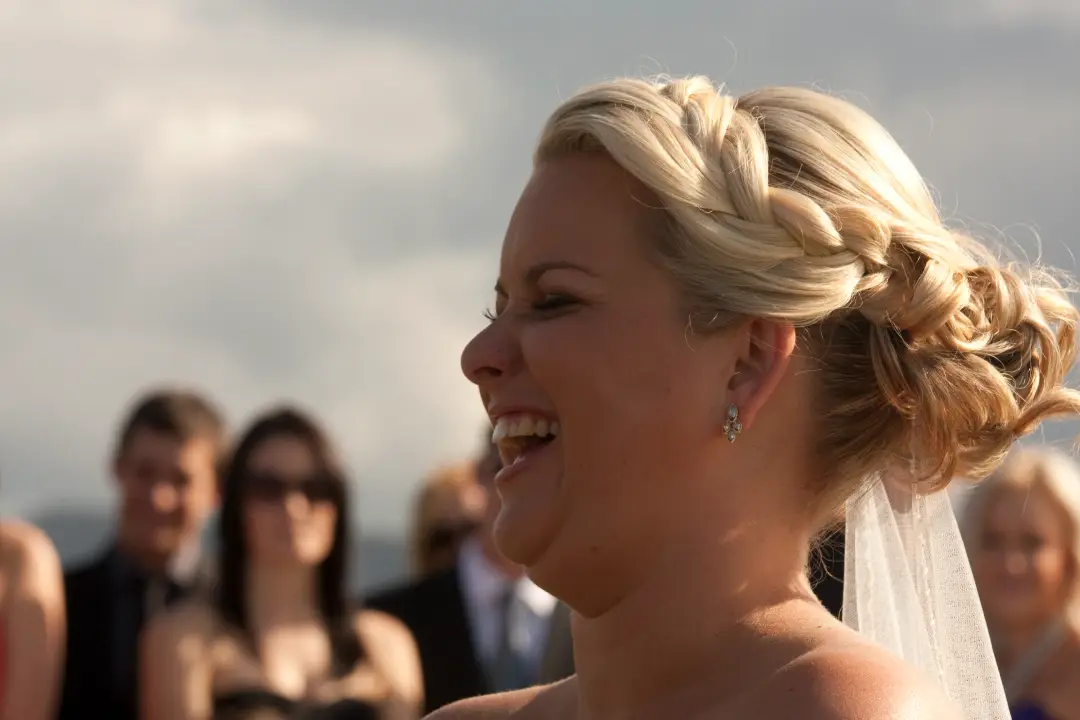 Bride laughing at her ceremony, her blonde hair twisted into a low updo with the veil pinned beneath