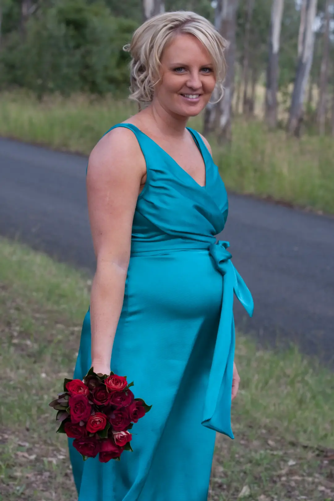 Mother of the bride in a teal gown with a short blonde style, holding red roses