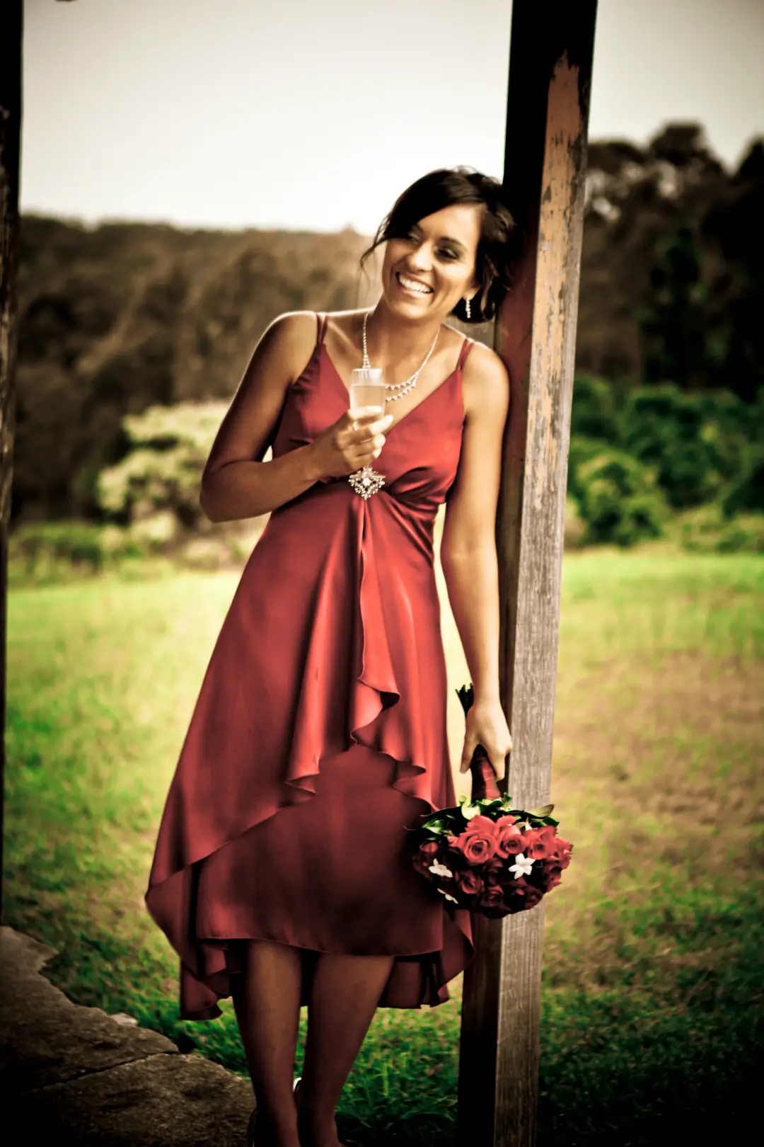 Bridesmaid in a red dress with her dark hair pinned back, holding a red rose posy