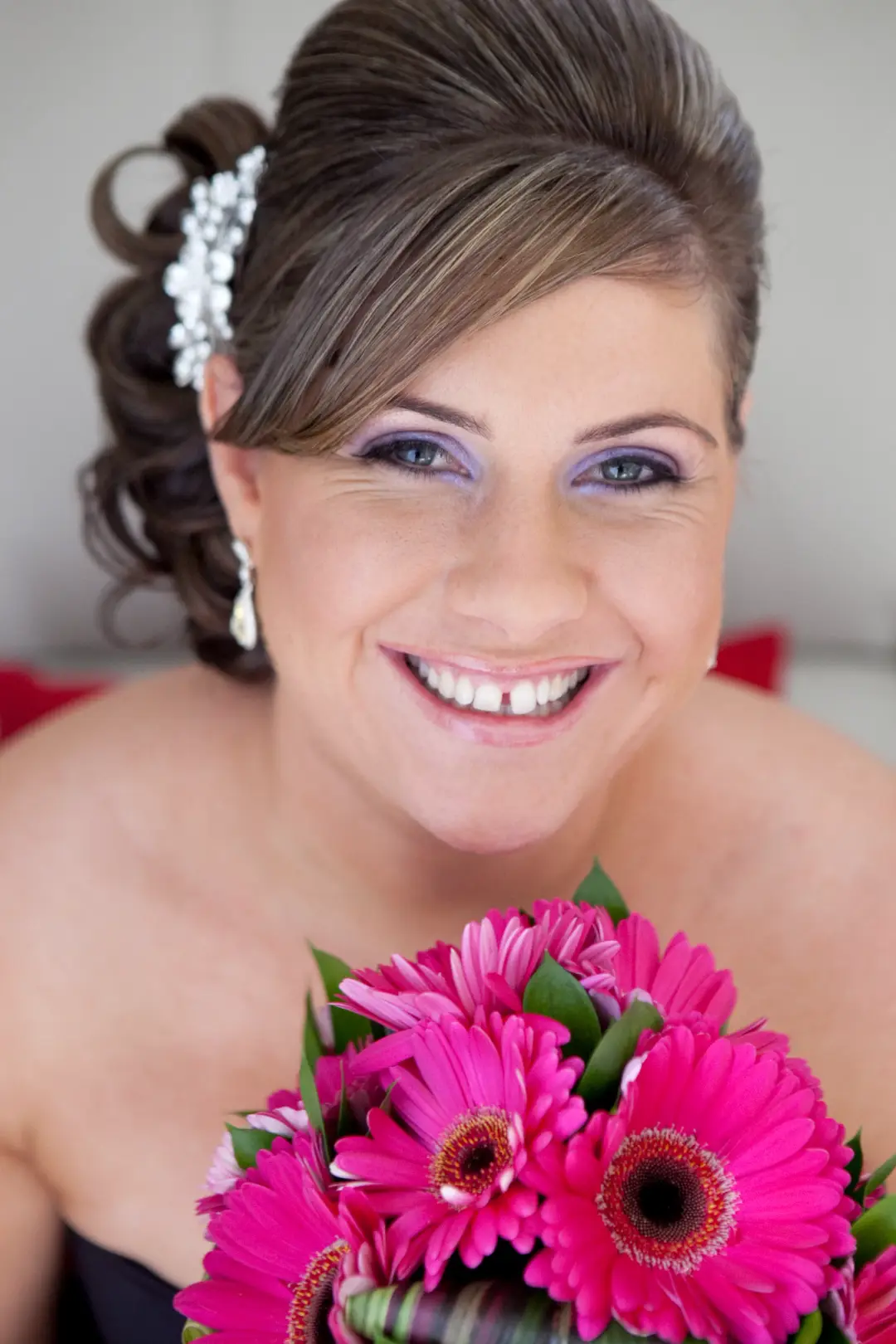 Bridesmaid in a curled half up style pinned with a diamante comb, holding pink gerberas