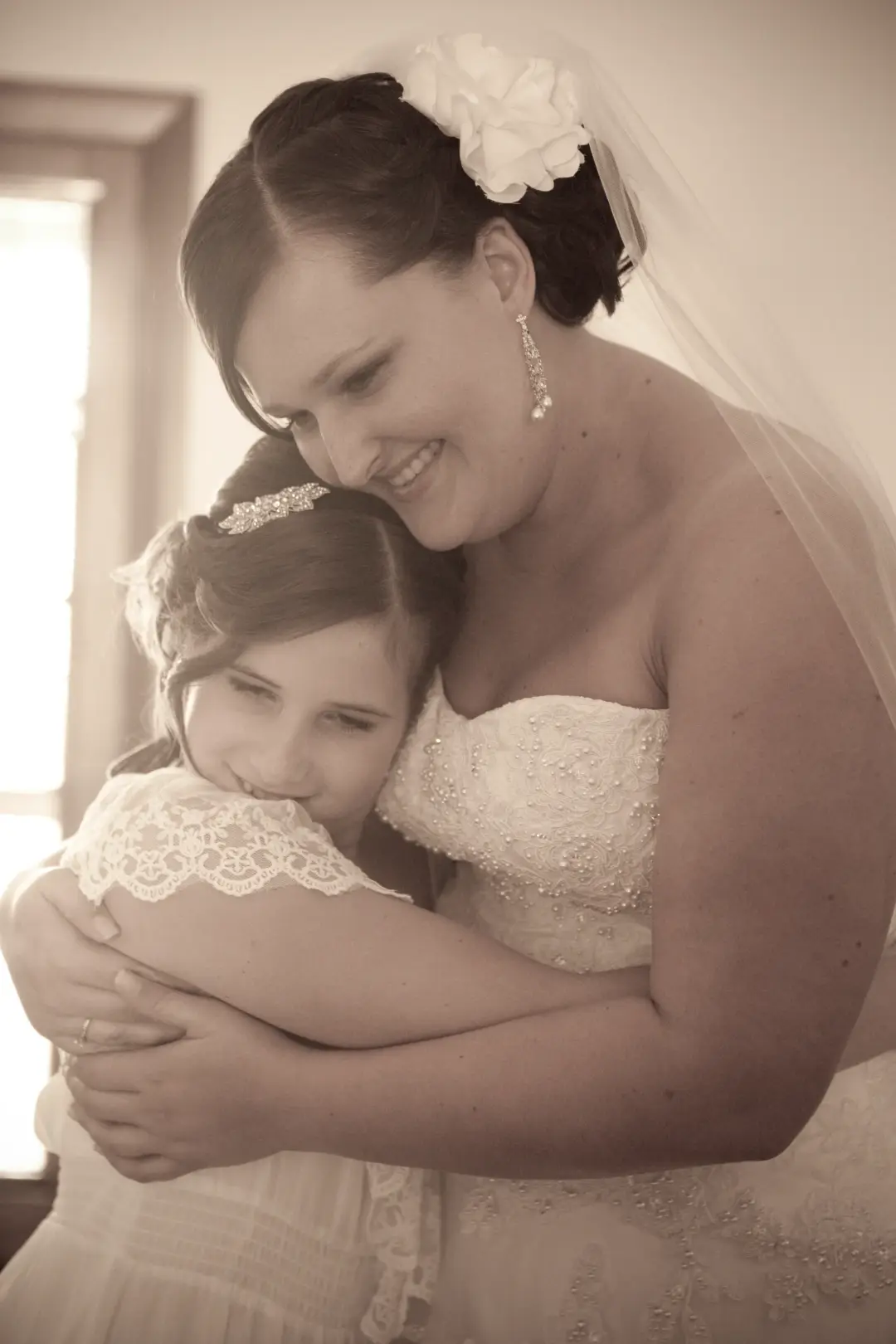 Bride holding her flower girl, wearing a white flower in a dark pinned style beneath her veil