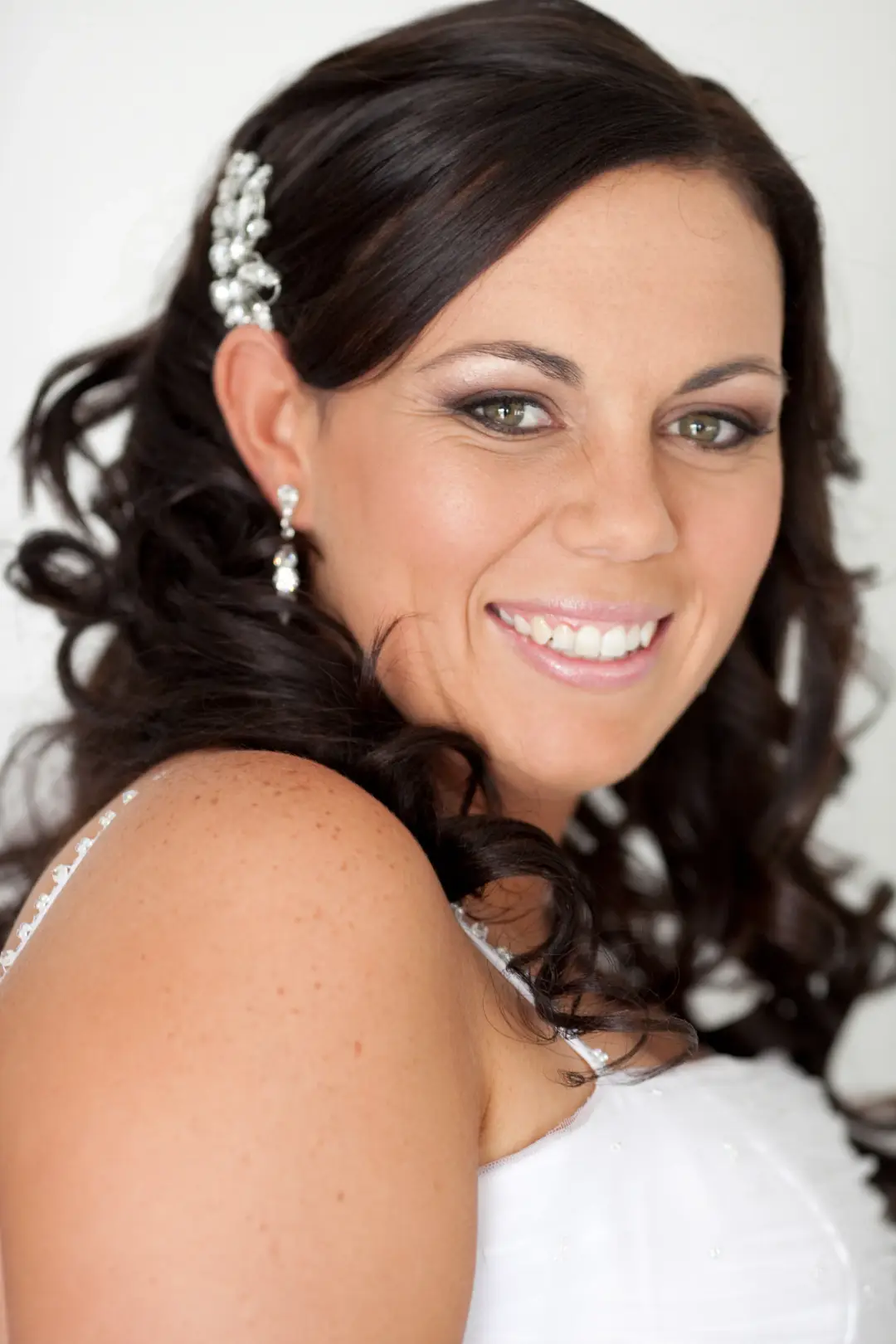 Bride with long dark curls worn to one side, pinned with a crystal comb and wearing warm bronze eye makeup