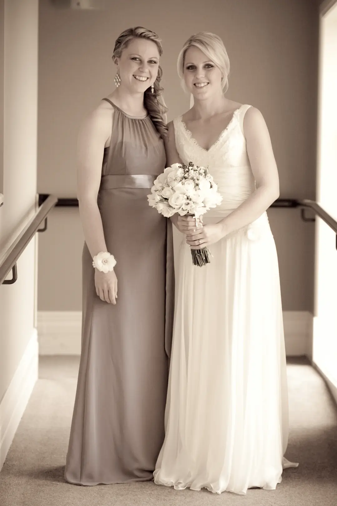 Bride and her bridesmaid on the stairs, both with their hair styled and pinned back