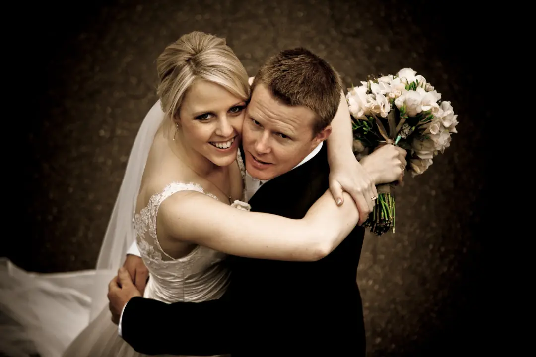 Bride and groom embracing, her blonde hair pinned into a curled updo under a veil