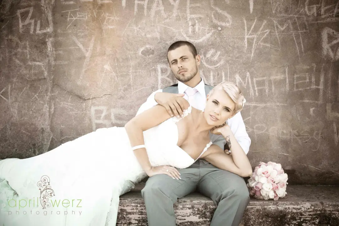 Bride and groom seated on a stone ledge, her blonde hair pinned into a low updo