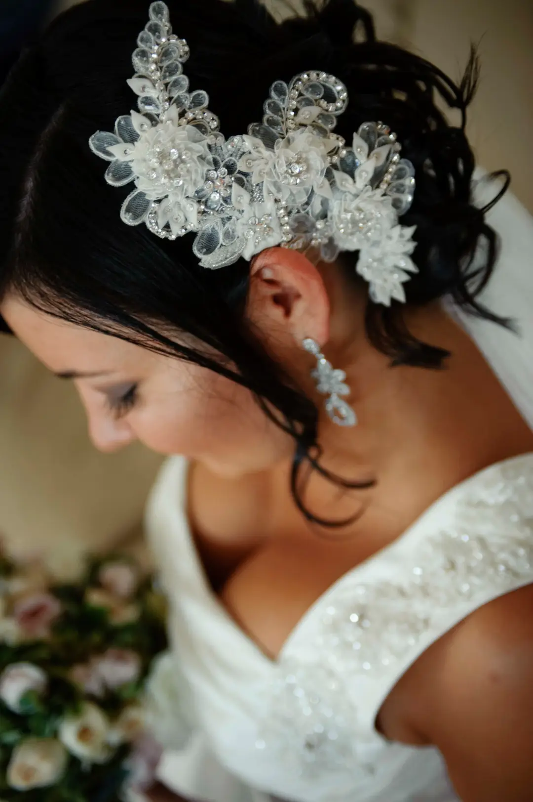 Ornate crystal and lace headpiece pinned into a dark bridal updo beside a beaded earring