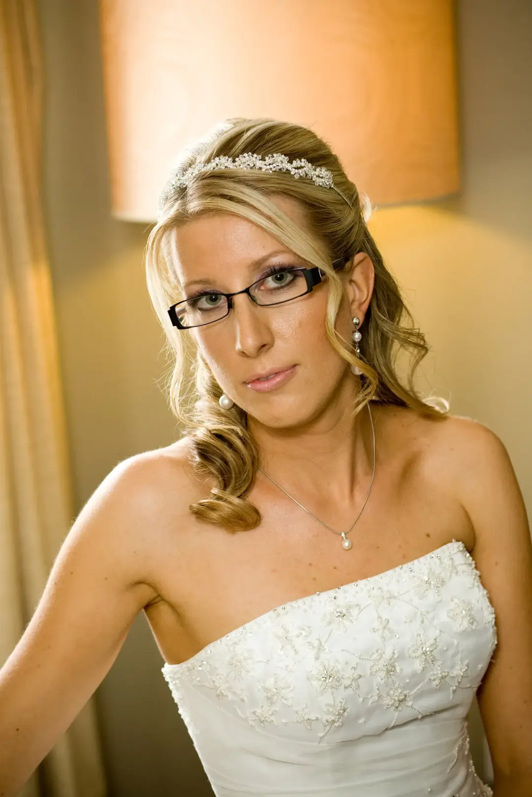 Bride in glasses with a tiara, her blonde hair curled and swept over one shoulder