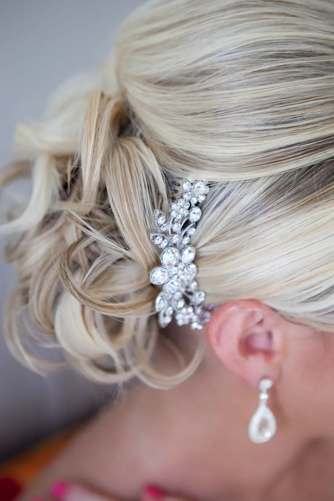 Crystal hair comb pinned into a soft blonde updo, worn with a pearl drop earring