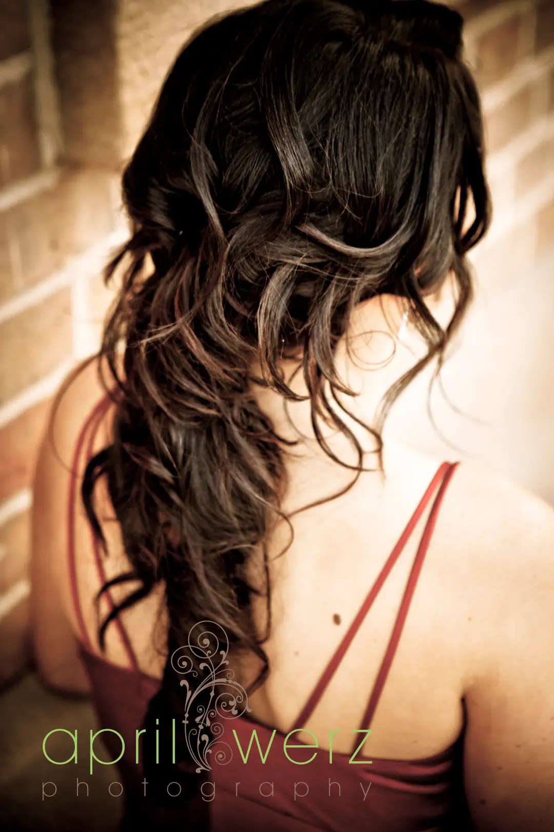 Back view of long dark hair styled into loose romantic curls swept over one shoulder