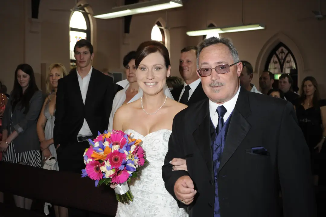 Bride walking down the aisle on her father's arm, her dark hair pinned into a low updo