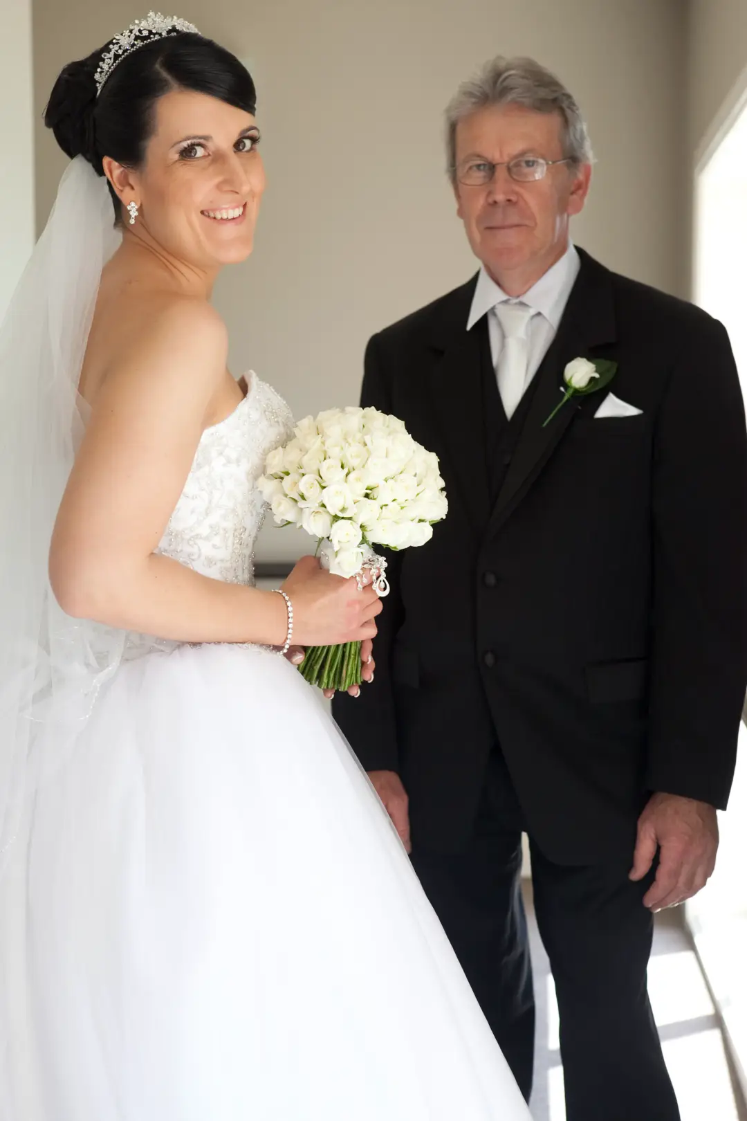 Bride with her father before the ceremony, her dark hair in a high updo under a tiara and veil
