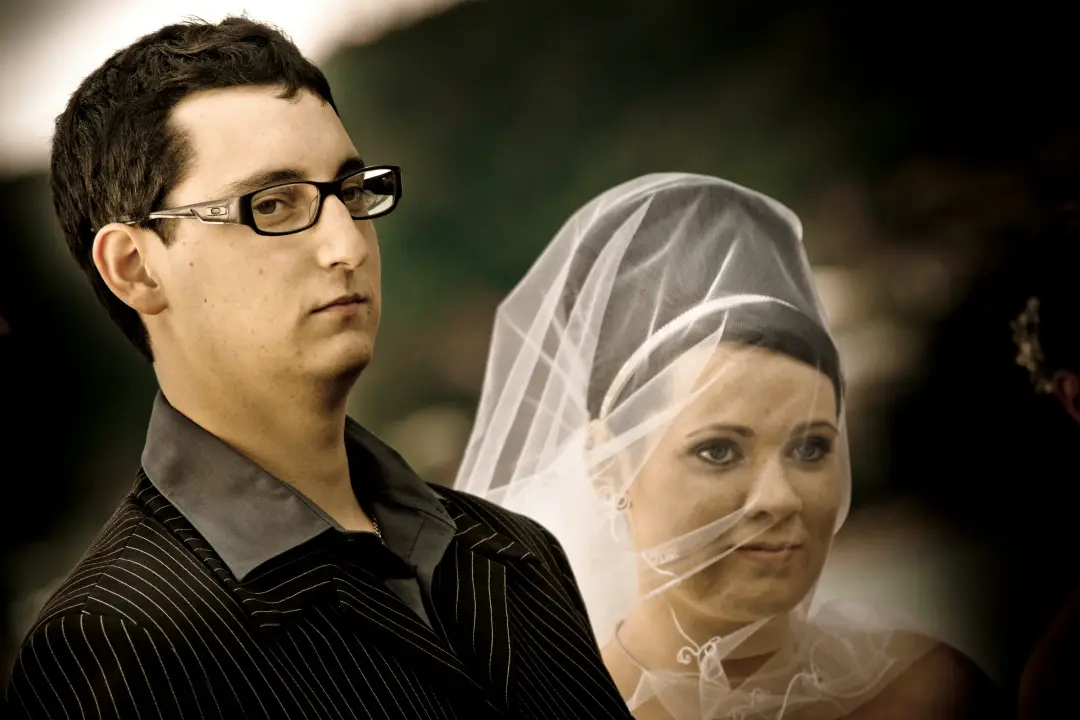 Bride under a fingertip veil beside her groom, her dark hair pinned smooth underneath